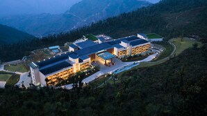 A modern hotel with multiple buildings, a swimming pool, and a mountainous backdrop.