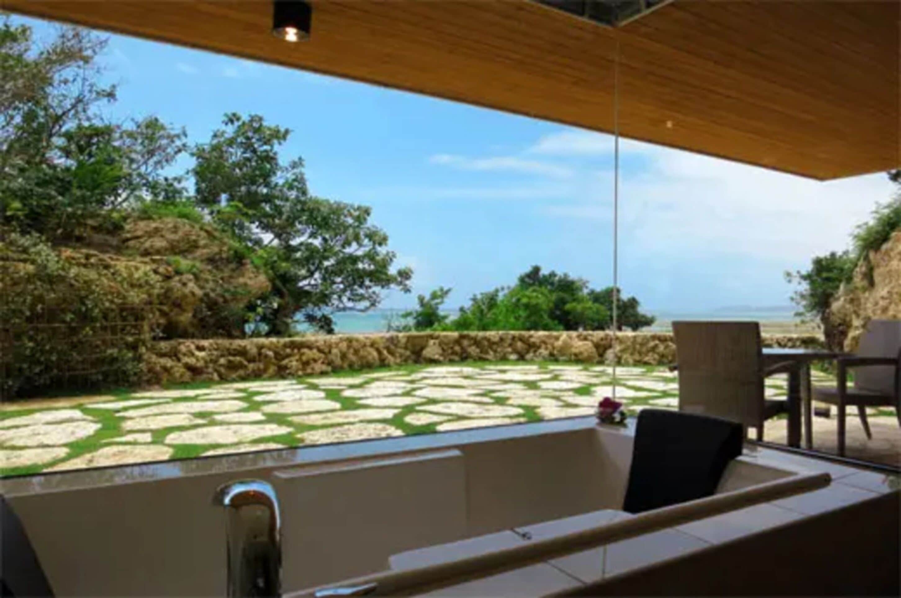 Un baño exterior moderno con suelo de baldosas de piedra, una bañera y una pérgola de madera.