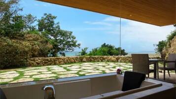 Un baño exterior moderno con suelo de baldosas de piedra, una bañera y una pérgola de madera.