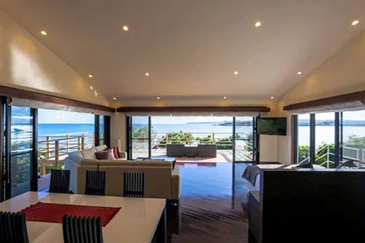 A spacious living area with a large window overlooking the sea, a dining table, and a seating area with a sofa and chairs.
