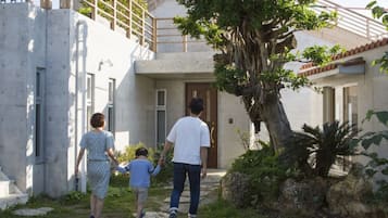 A family walking towards a house with a stone pathway, a large tree, and a wooden fence.