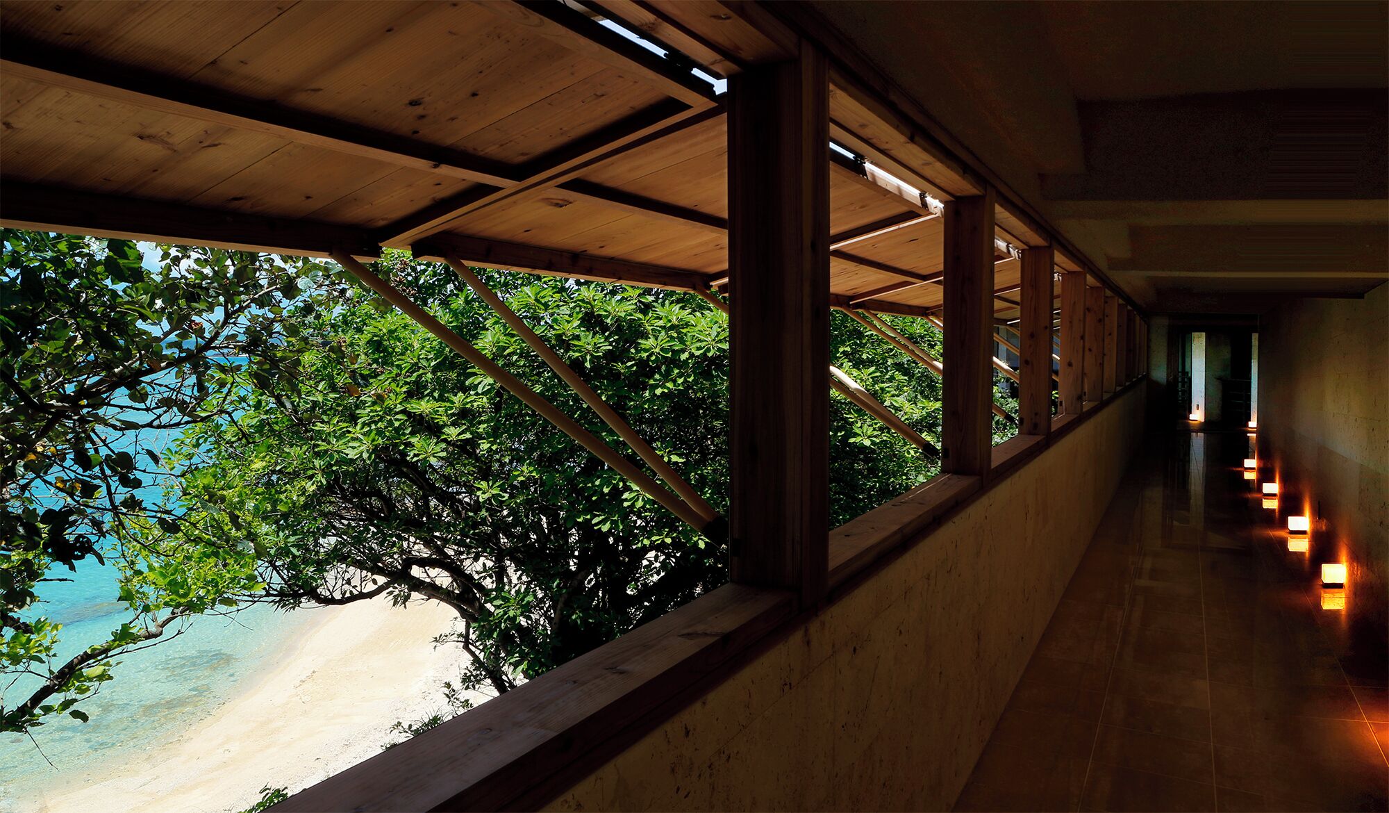 A corridor with wooden beams and large windows overlooking a beach.