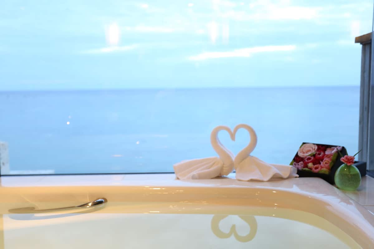 A bathtub with a heart-shaped towel arrangement and a bouquet of flowers.