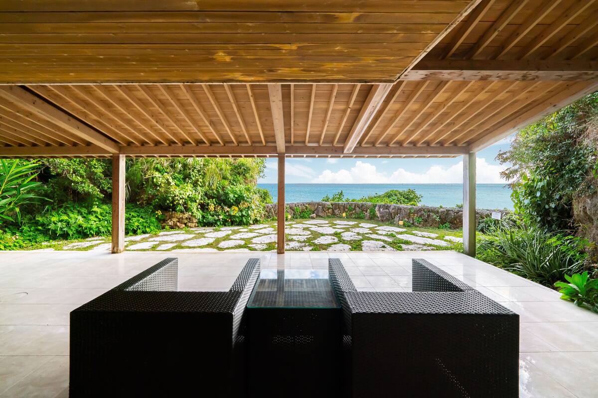 An outdoor patio with a wooden pergola, a glass-top table, and a view of the ocean.