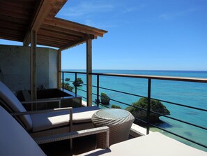 Un balcon agrémenté de meubles en osier, une vue sur la mer et un ciel dégagé.