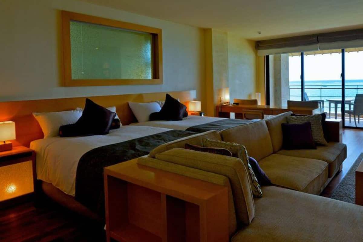 A hotel room with a bed, a sofa, a desk, and a large window with a view.