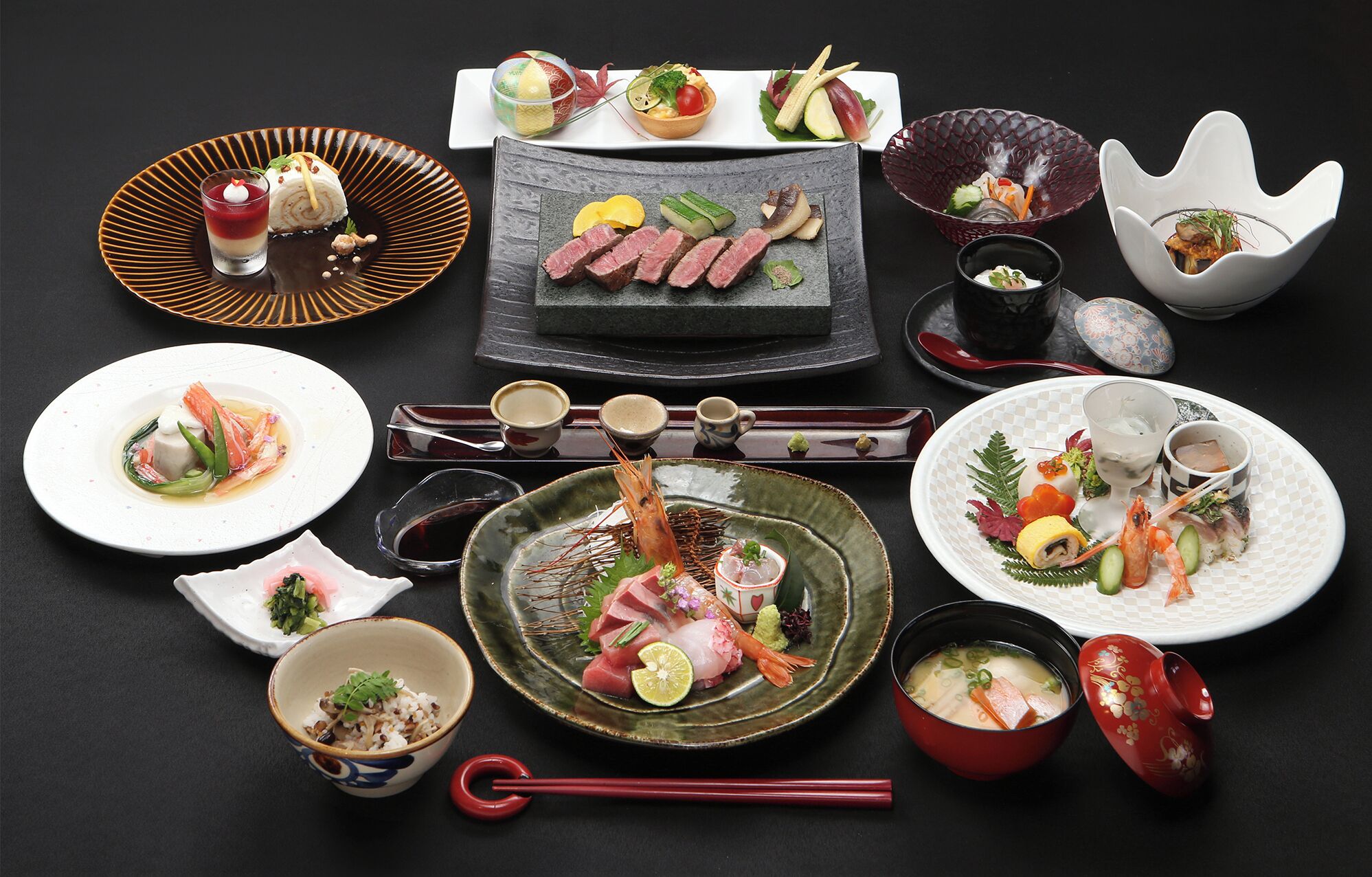A variety of Japanese dishes arranged on a table, including sushi, sashimi, and a bowl of soup.