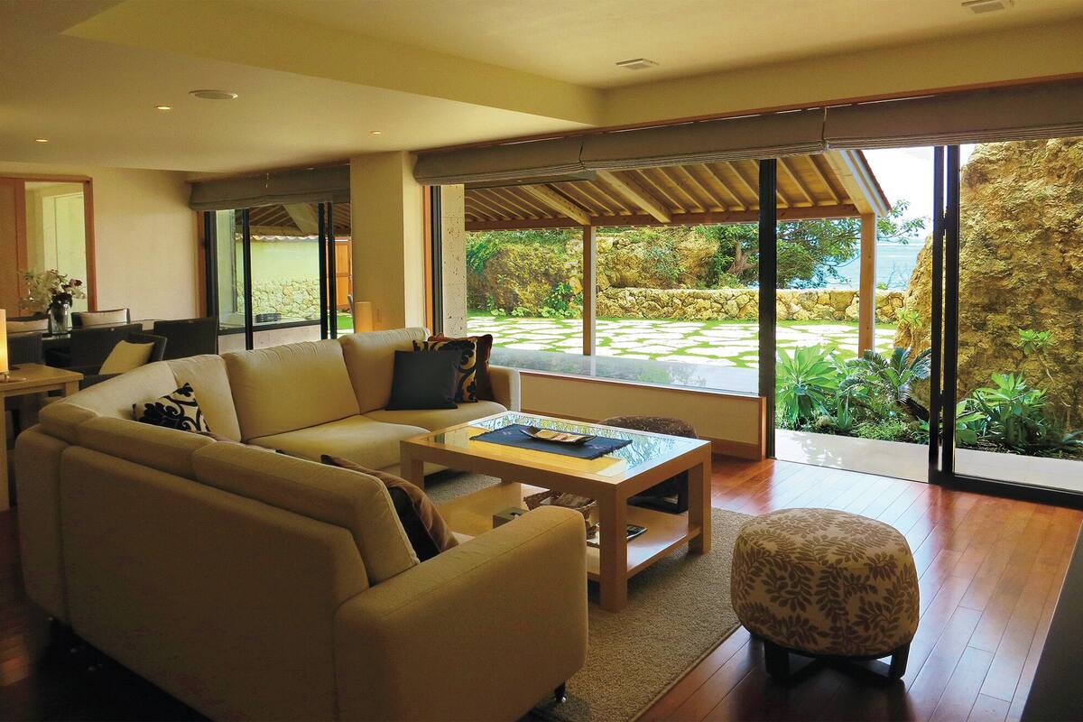 A modern living room with a sofa, coffee table, and ottoman. There is a large window providing a view of the outdoors.