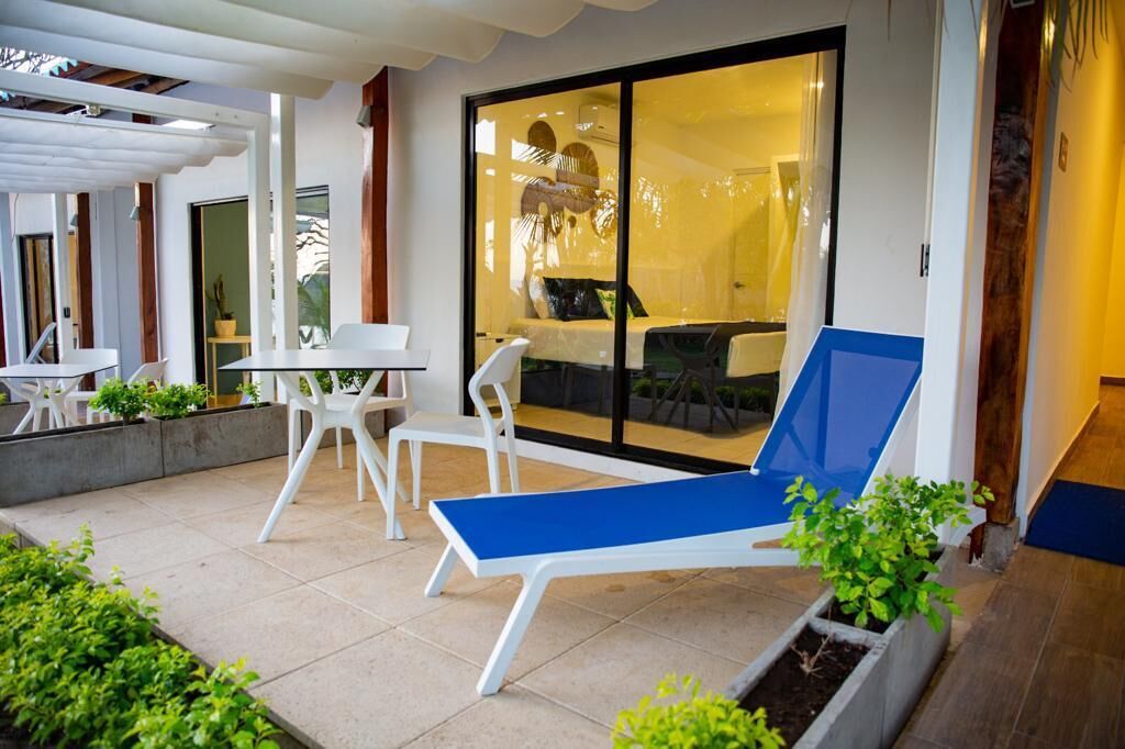 Un patio moderno al aire libre con una silla reclinable azul, sillas blancas y una pequeña mesa.