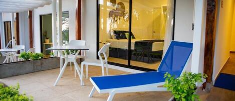 Un patio moderno al aire libre con una silla reclinable azul, sillas blancas y una pequeña mesa.
