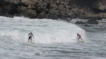 Zwei Surfer auf einer Welle mit einer felsigen Küstenlinie im Hintergrund.