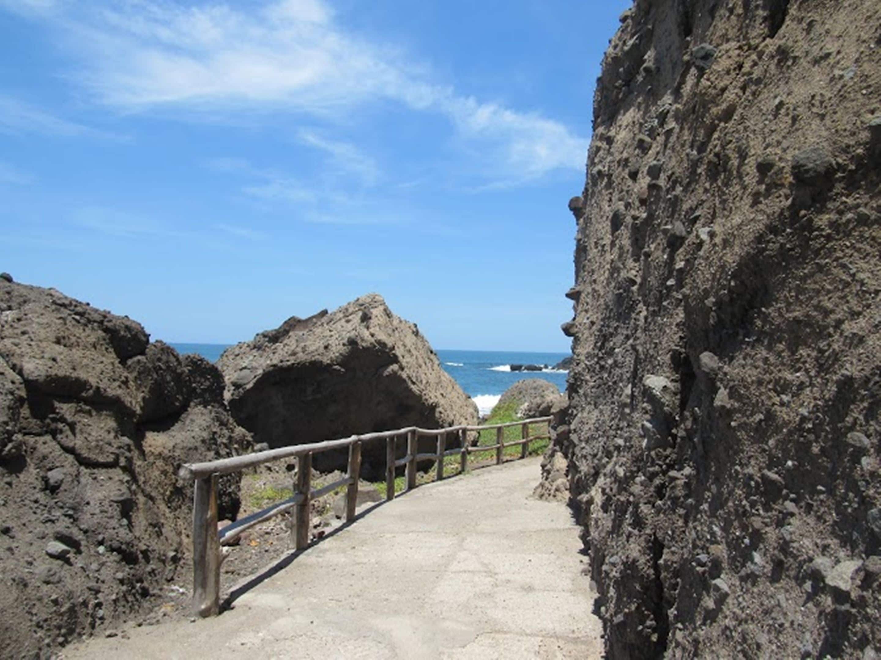 A concrete pathway with a wooden railing leading to a rocky cliff overlooking the ocean.