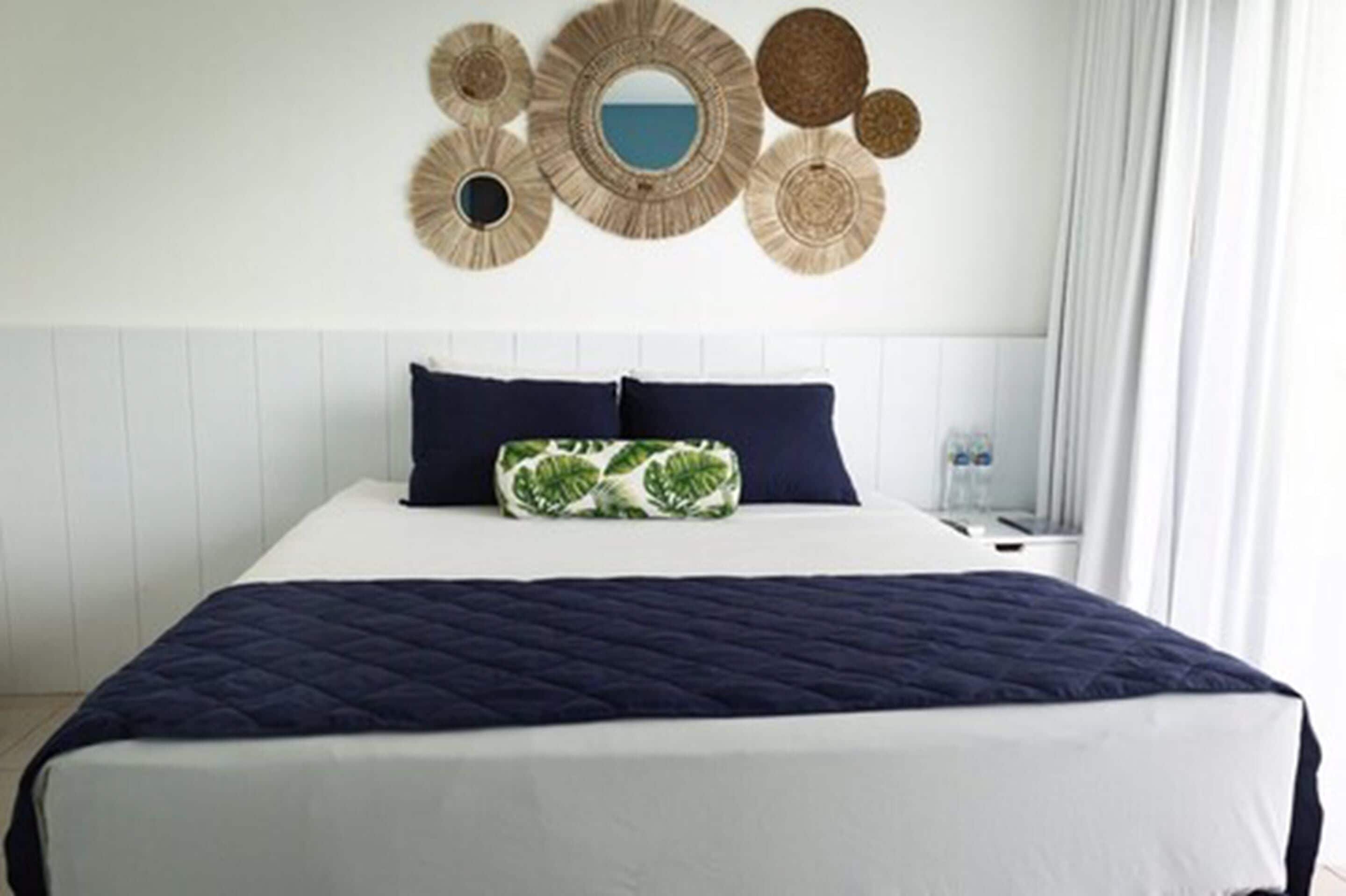 Een hotelkamer met een groot bed, een wit hoofdbord en een decoratief kunstwerk erboven.