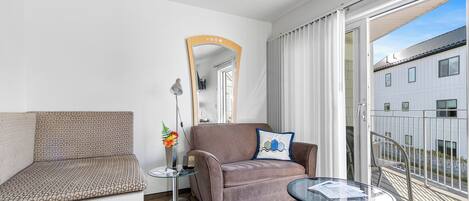 Una habitación de hotel moderna con sofá, una mesita, un espejo y un balcón con vistas a un edificio.