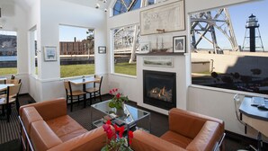 Una habitación moderna con chimenea, sofás de cuero, zona de comedor y grandes ventanales con vistas a un puente y al agua.