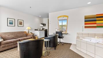 A hotel room with a sofa, two chairs, a desk, a mirror, a bathroom with a bathtub, and a city view.