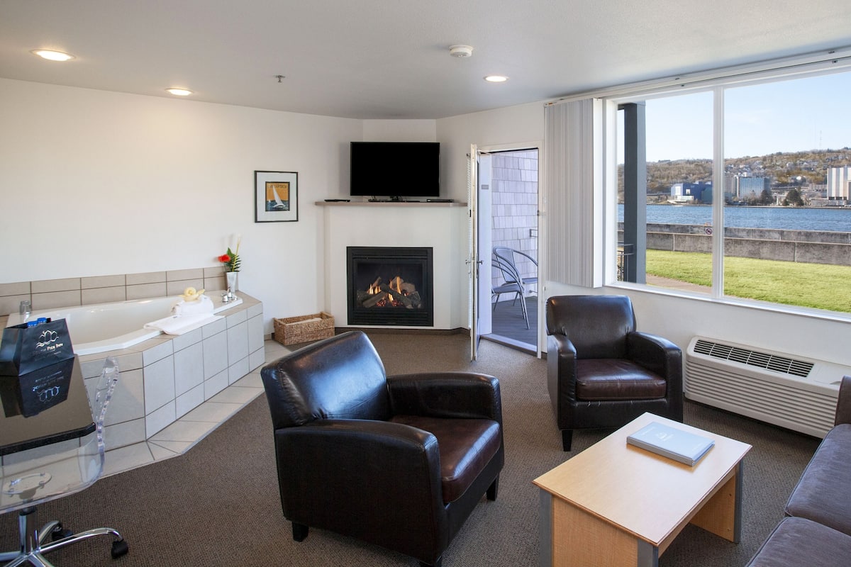 A modern living room with a fireplace, leather sofas, a coffee table, and a large window overlooking a body of water.