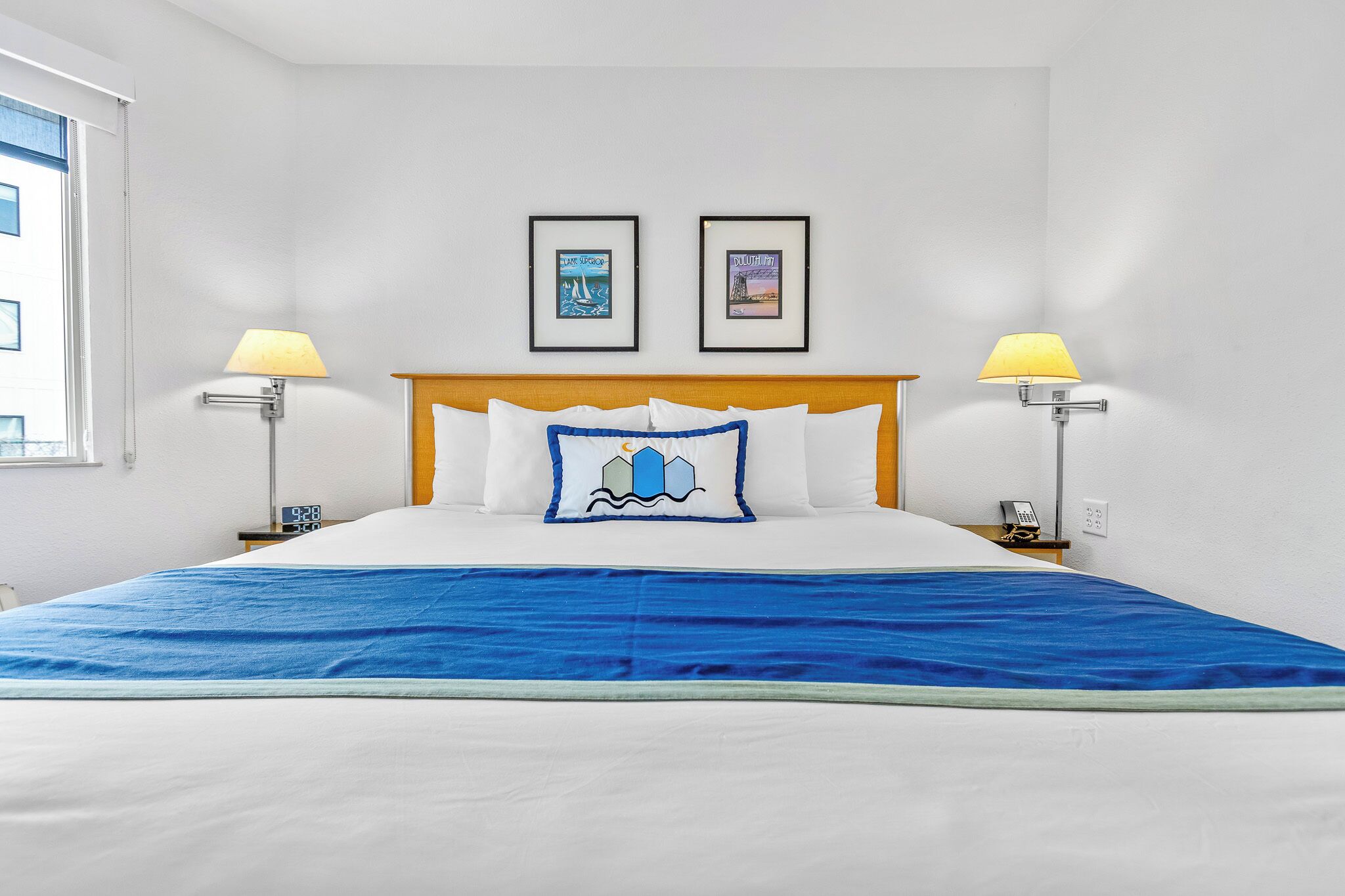 Una habitación de hotel con una cama, dos cuadros en la pared, una lámpara de noche y un reloj.