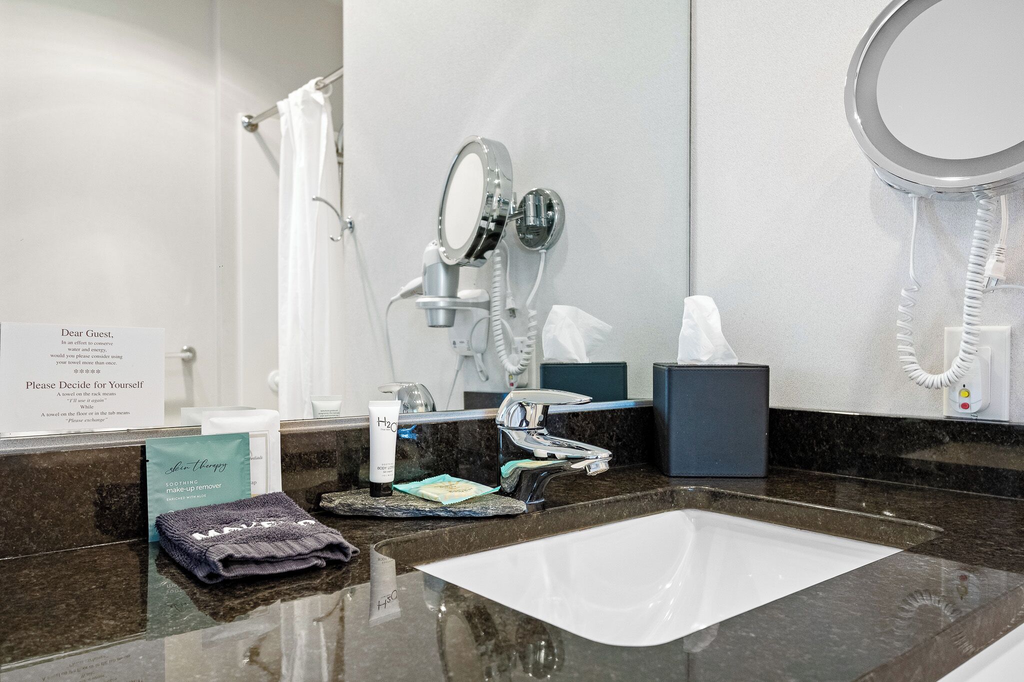 Baño de hotel con lavabo, espejo, toallero y un cartel sobre el uso de toallas.