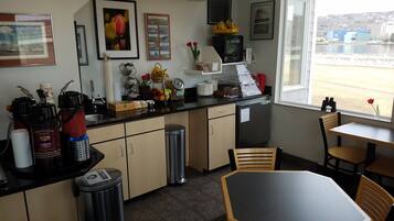 Une cuisine équipée d’une machine à café, d’une poubelle et d’une fenêtre donnant sur des immeubles.