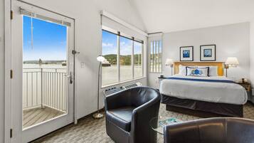 Habitación de hotel con cama, dos sillas, escritorio, ventana con vista al mar y puerta que da a un balcón.