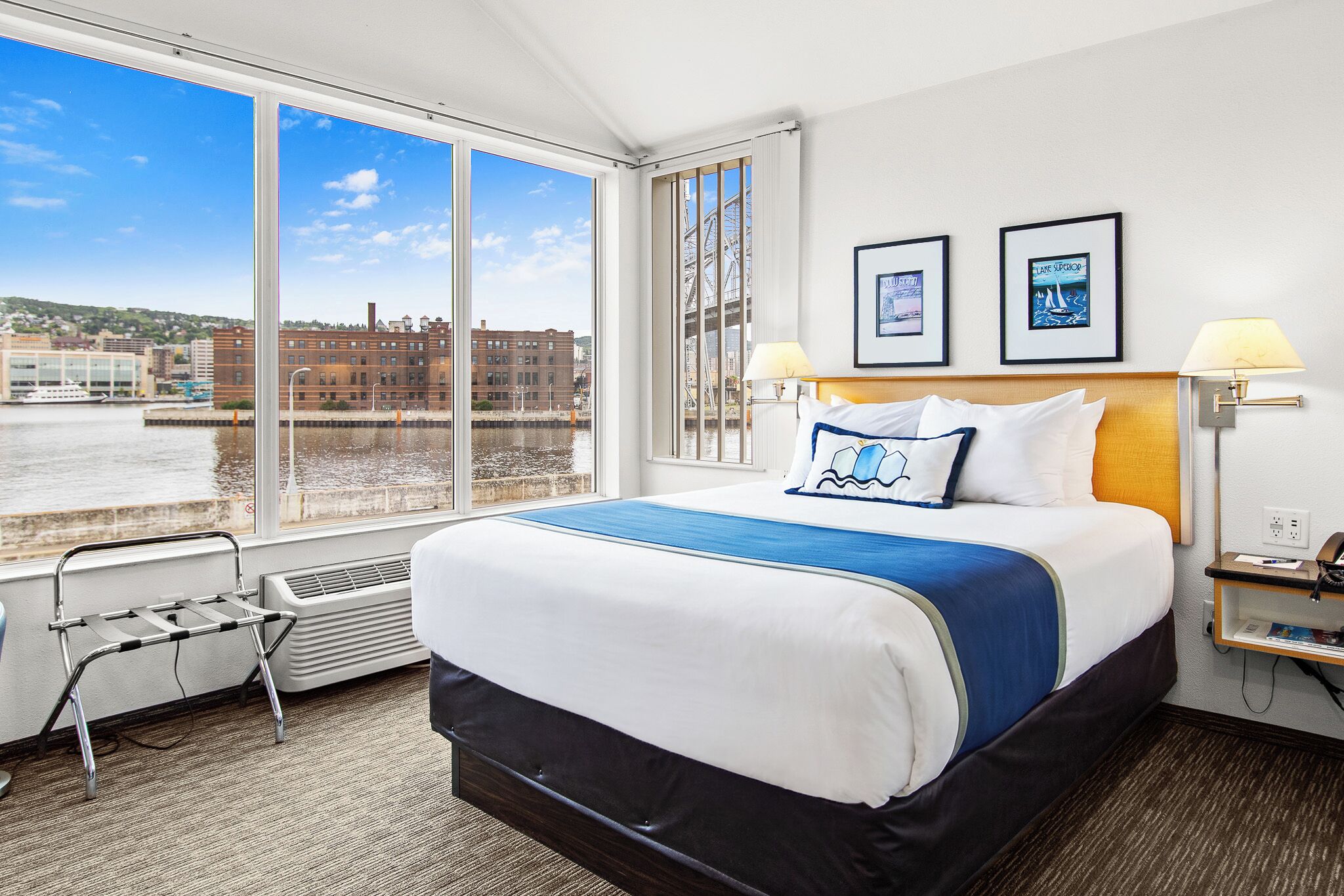 A hotel room with a large bed, a view of the water and buildings, and two framed pictures on the wall.