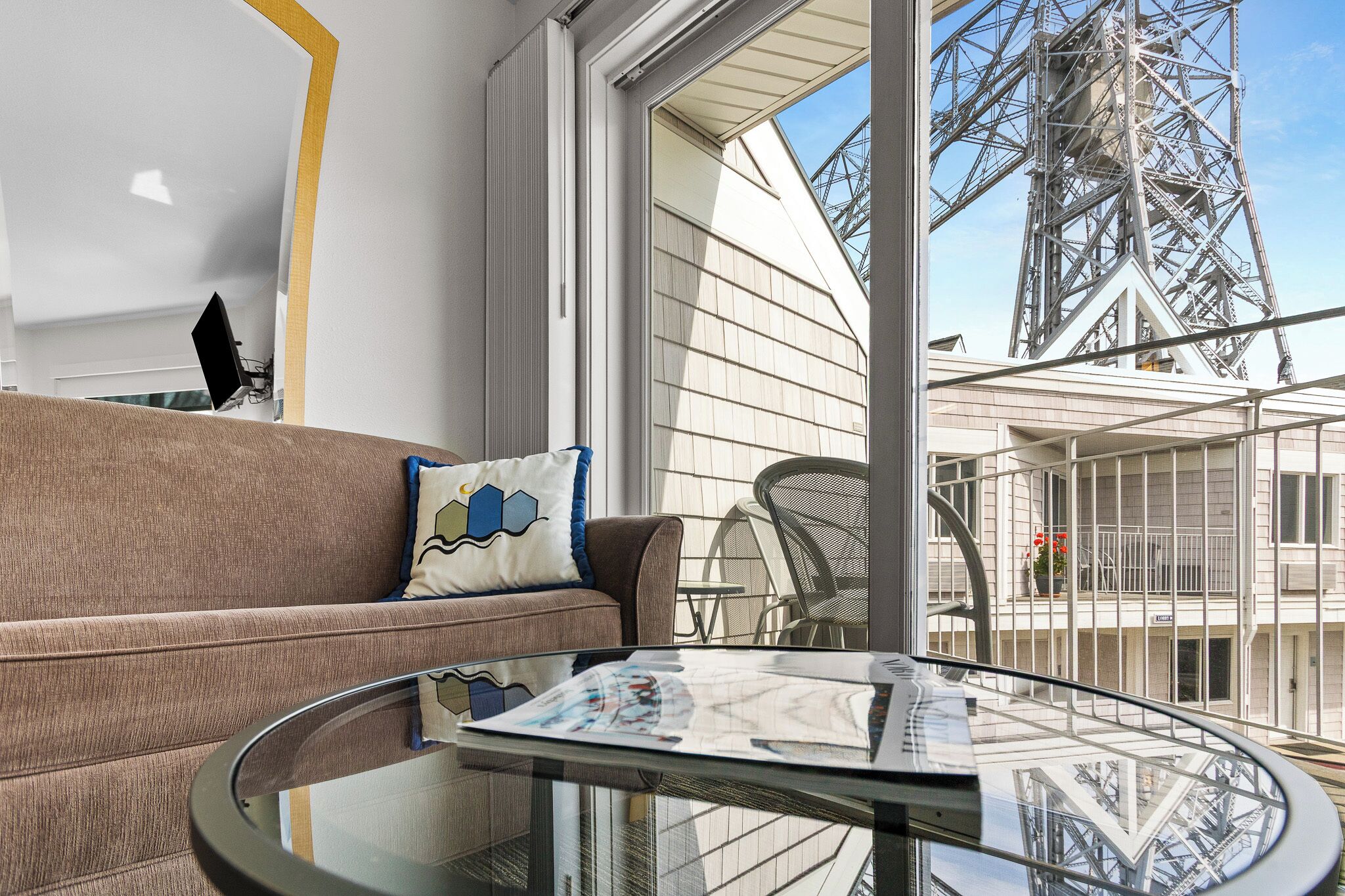 A modern interior with a sofa, a glass table, and a view of a large metal structure outside.