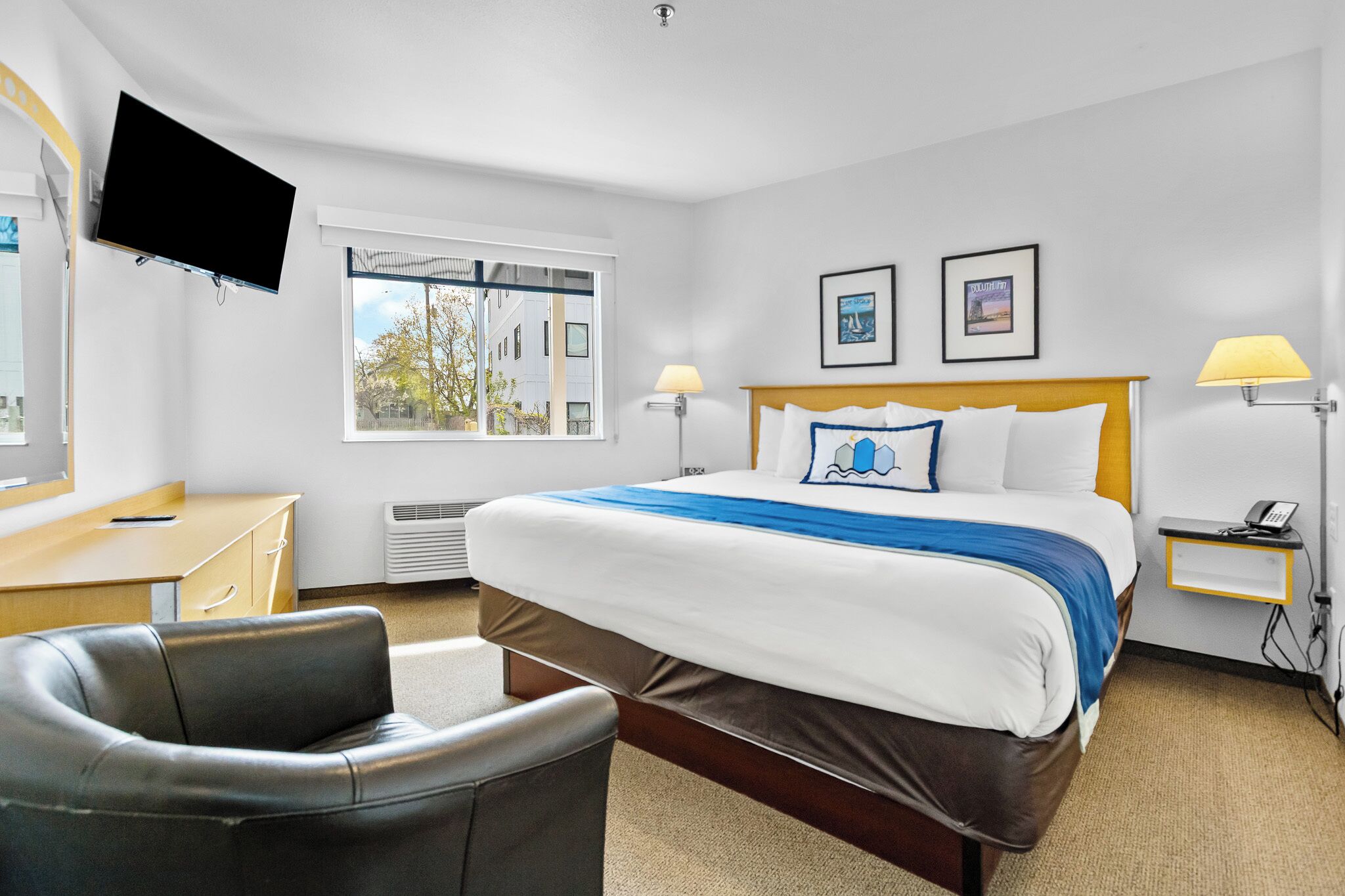 A hotel room with a bed, desk, chair, TV, and two framed pictures on the wall.