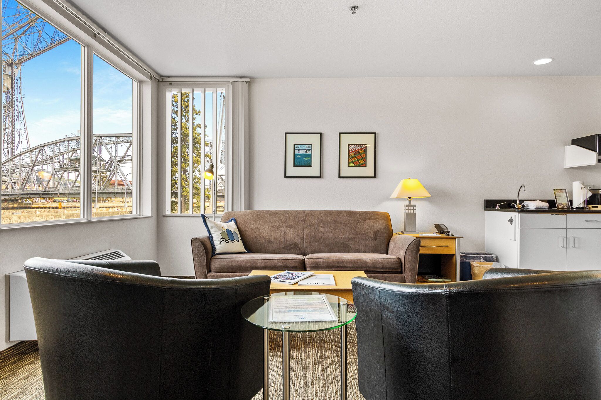 A modern living room with a sofa, two armchairs, a coffee table, and a view of a construction site through large windows.