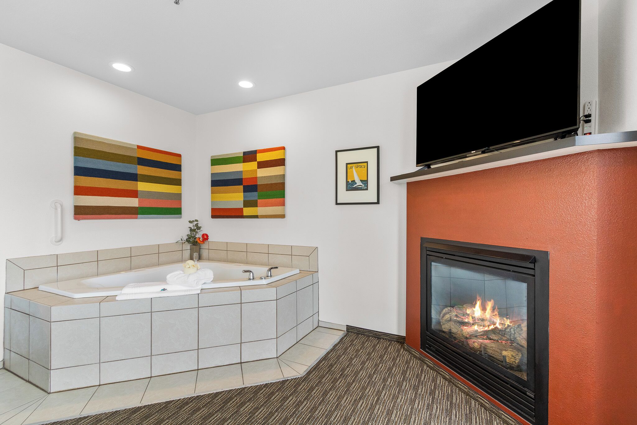 A modern bathroom with a large bathtub, a fireplace, and two colorful abstract paintings on the wall.