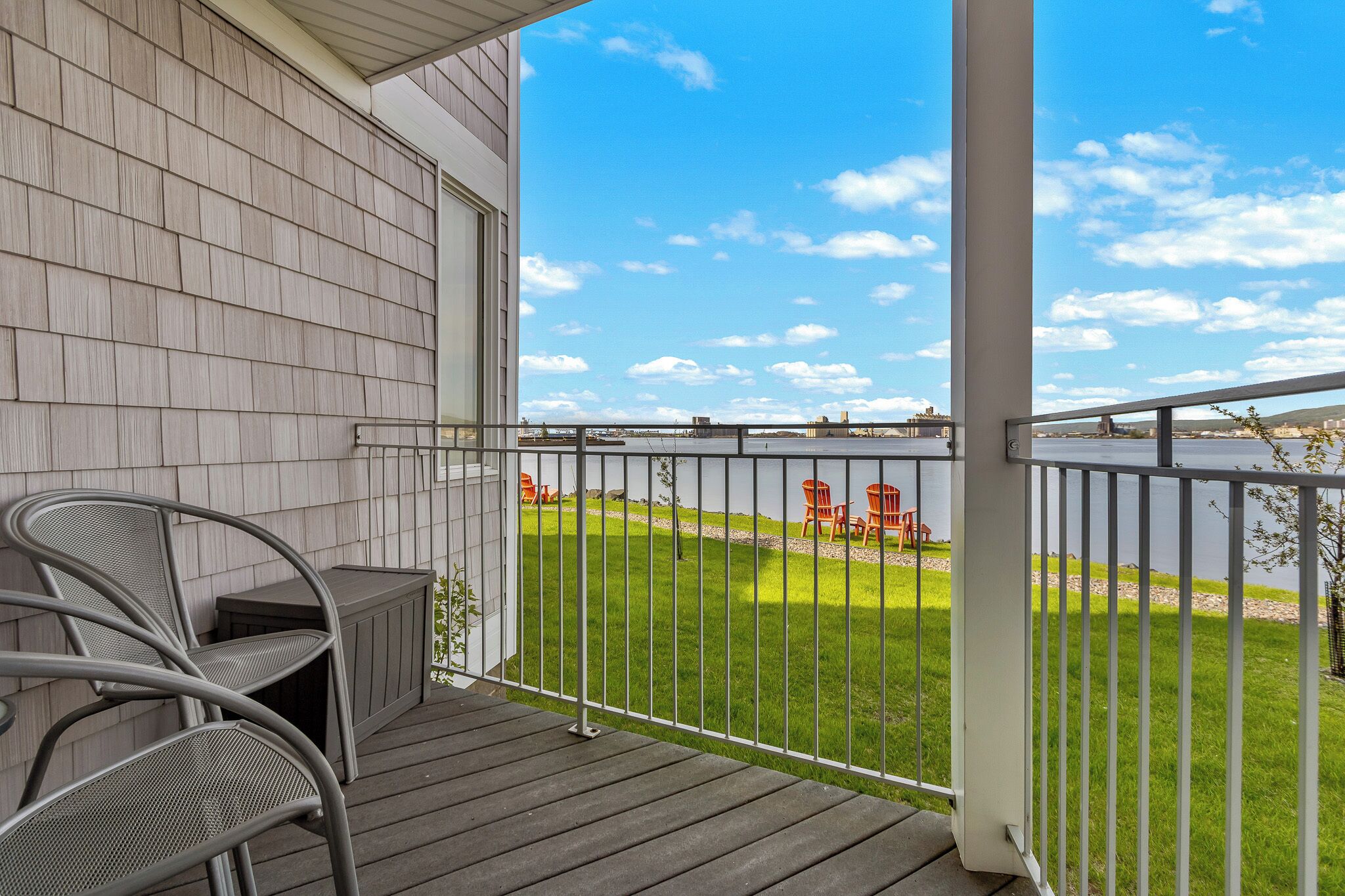 A covered outdoor area with a view of a body of water, a grassy lawn, and a metal railing.