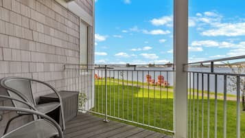 A covered outdoor area with a view of a body of water, a grassy lawn, and a metal railing.
