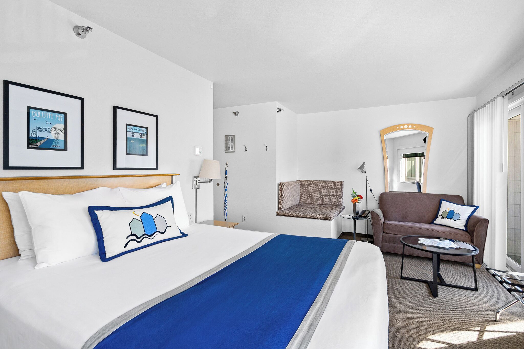 A hotel room with a bed, a sofa, a chair, a small table, and a mirror.
