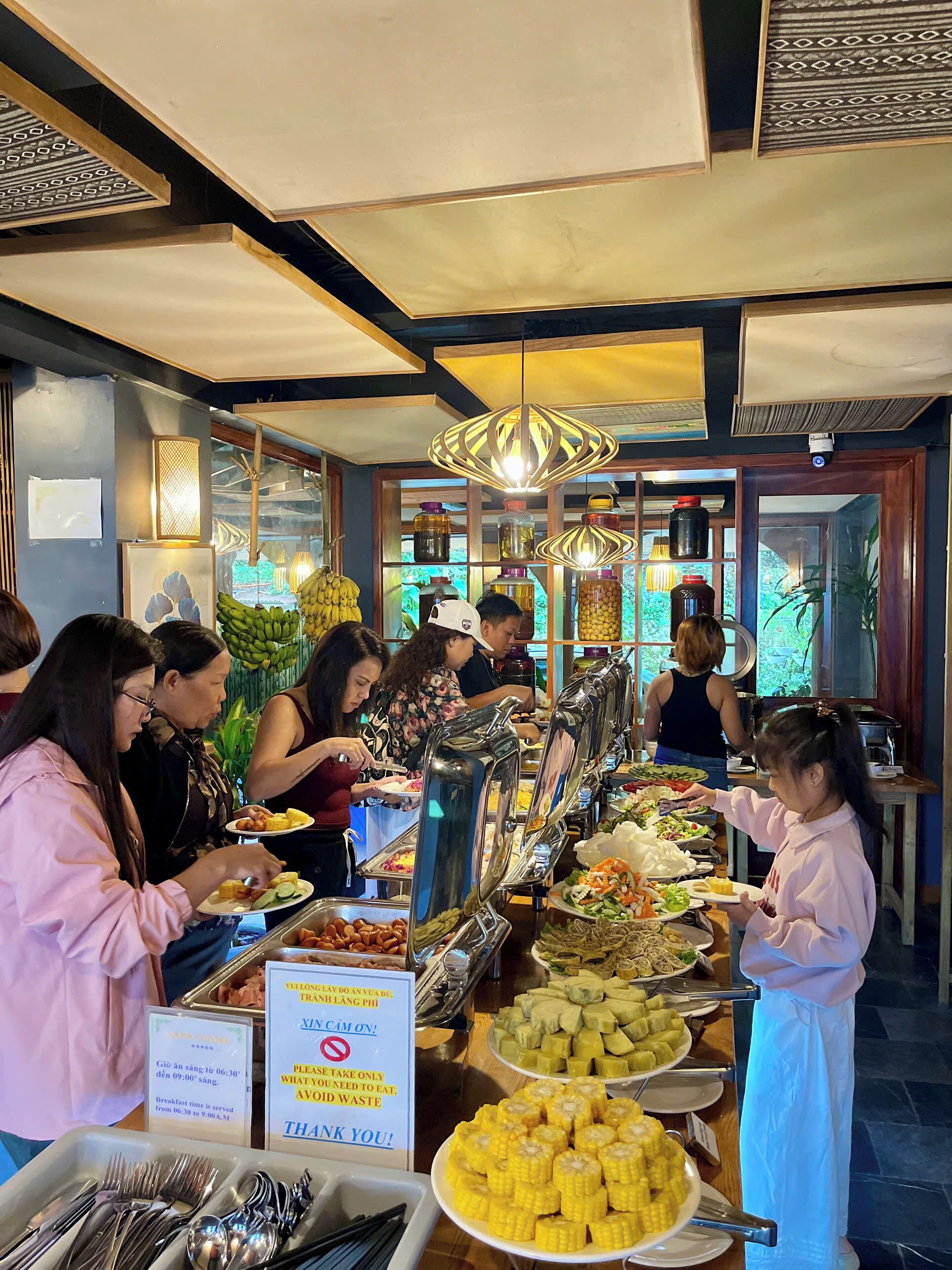 A buffet setup with various food items and a sign indicating breakfast hours.