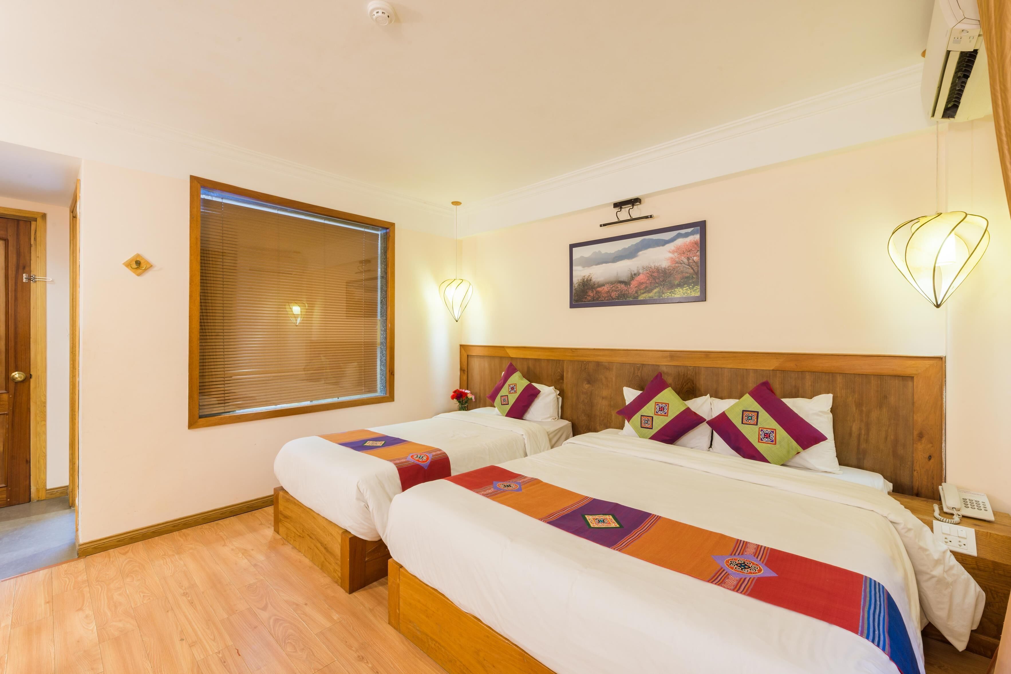 Habitación de hotel con dos camas, cabecero de madera, ventana con persianas, un cuadro colgado en la pared y teléfono en la mesita de noche.
