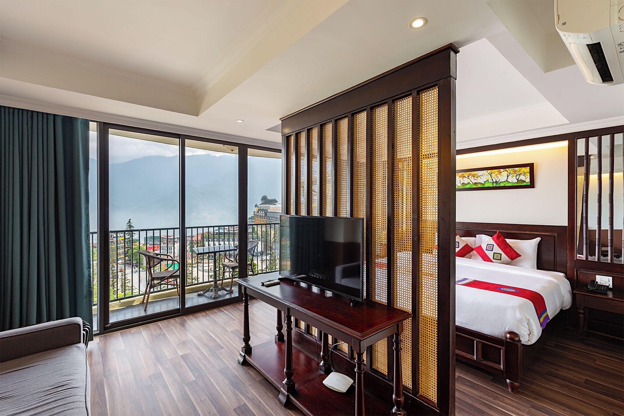 A hotel room with a balcony, a TV on a wooden table, a bed with white bedding, and a painting on the wall.