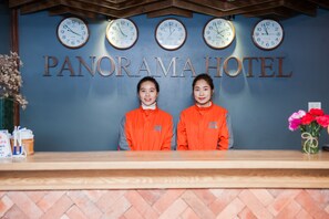 A reception desk at the Panorama Hotel with multiple clocks on the wall and two staff members in orange uniforms. - Sapa Panorama Hotel (Sa Pa)