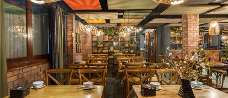 Een restaurant met houten tafels en stoelen, hangende kroonluchters en bakstenen muren.