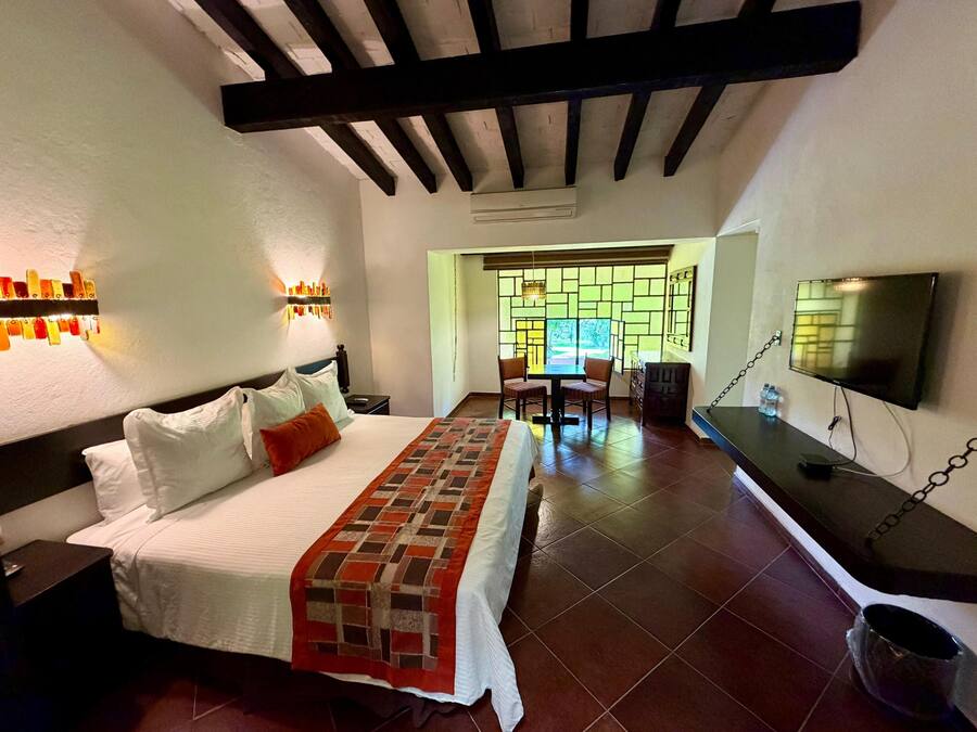 A hotel room with a bed, bedside table, TV, and a dining area with chairs and a table.