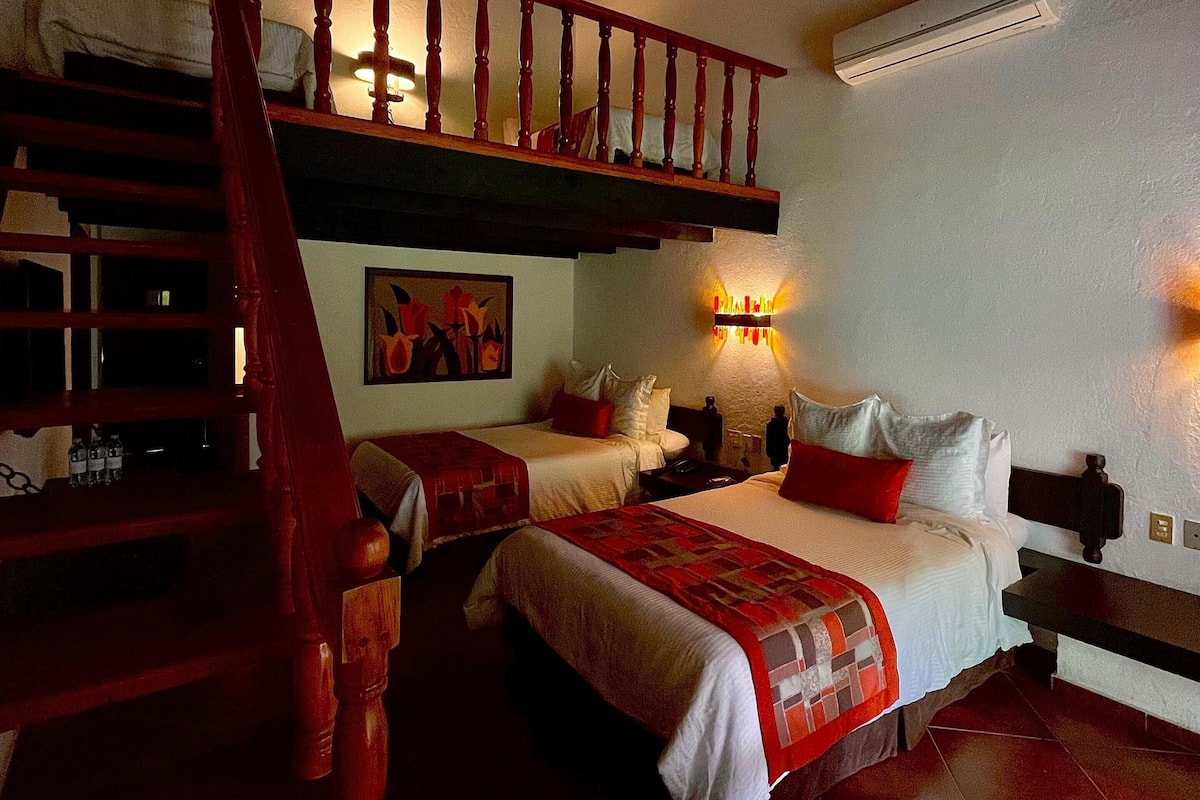 Une chambre d’hôtel avec un escalier en bois, deux lits, un tableau et un appareil de climatisation.
