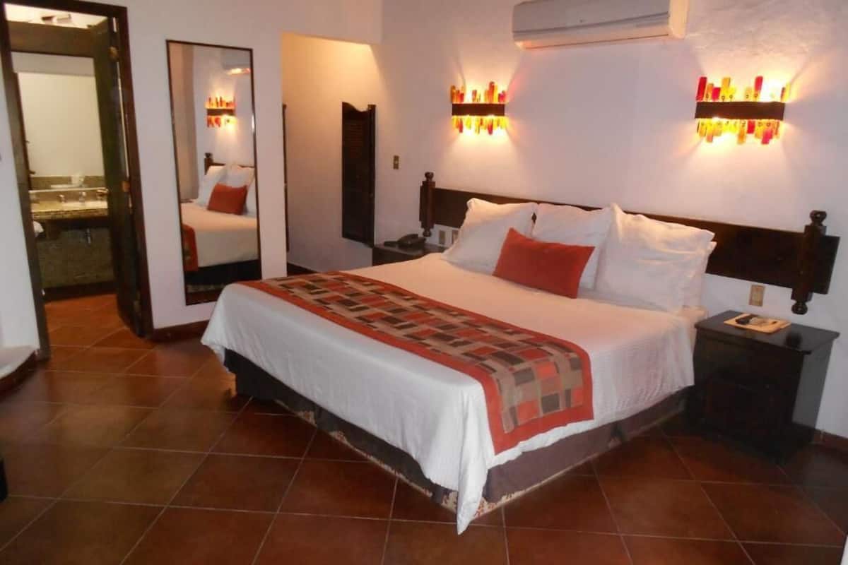 Une chambre d’hôtel avec un grand lit, une table de chevet, un miroir et des lampes fixées au mur.