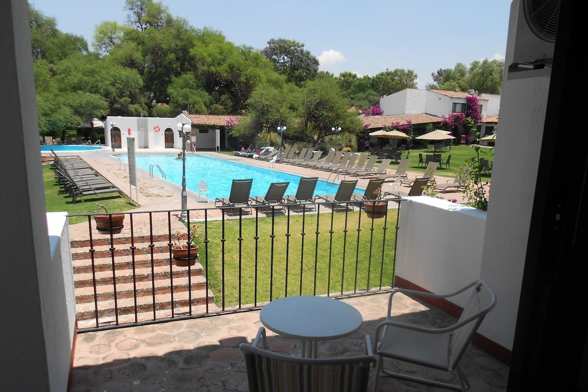 Un balcon avec vue sur une piscine, un espace salon extérieur et un jardin.