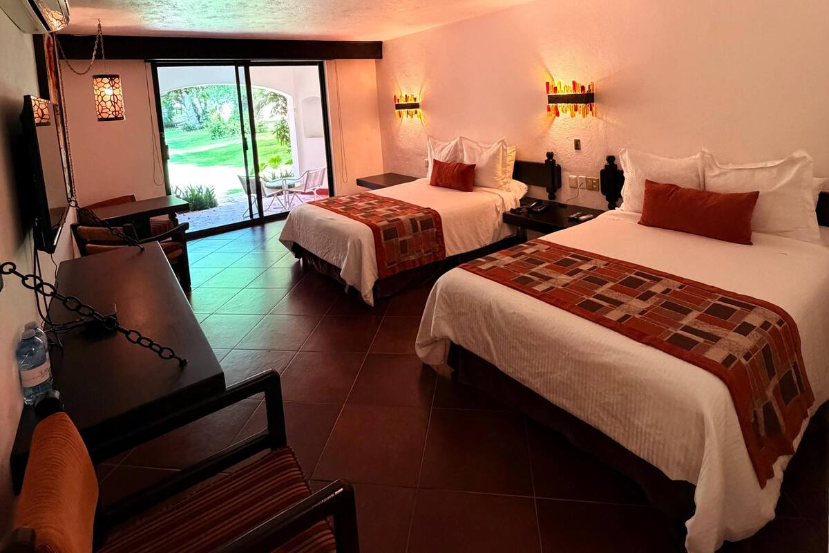 Une chambre d’hôtel avec deux lits, une table à manger, des chaises, une bouteille d’eau et une vue sur l’extérieur.