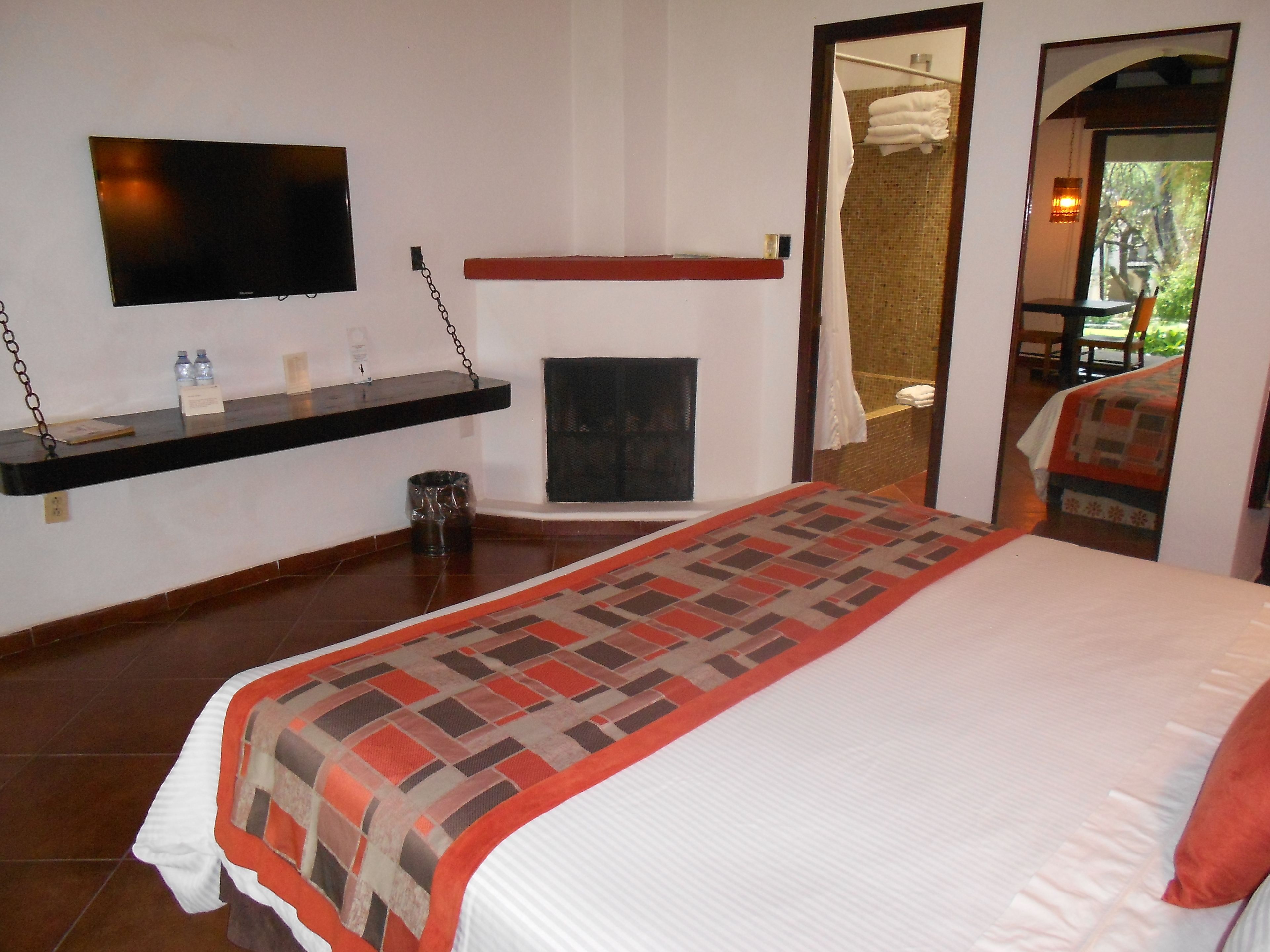 Habitación de hotel con cama, televisor montado en la pared, una pequeña repisa con artículos de aseo y vistas al exterior a través de una puerta.