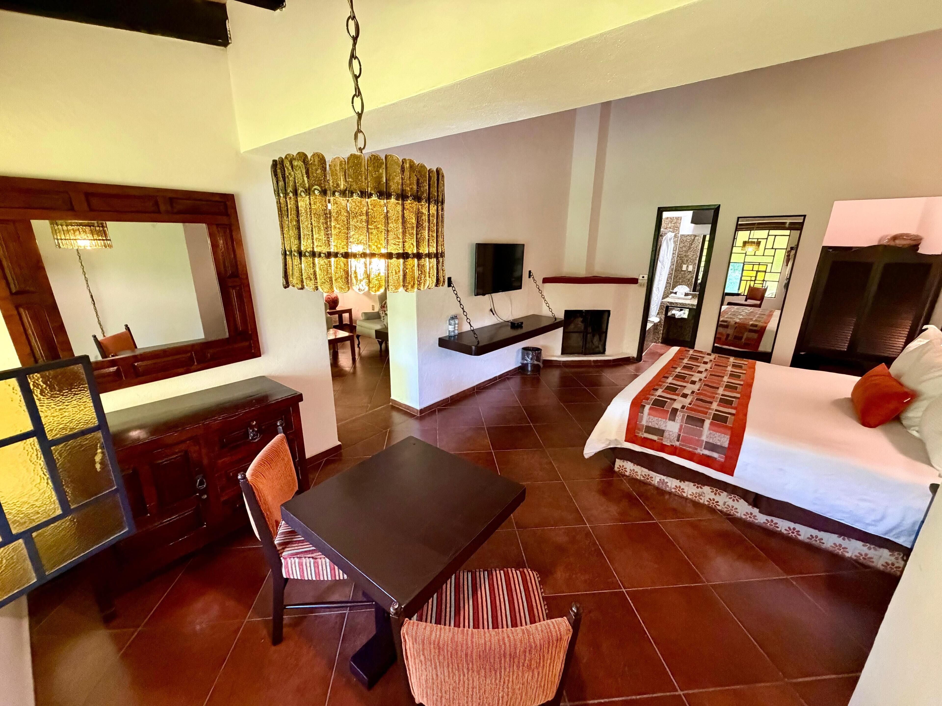 A hotel room with a bed, a dining table, a chair, a TV, and a fireplace.