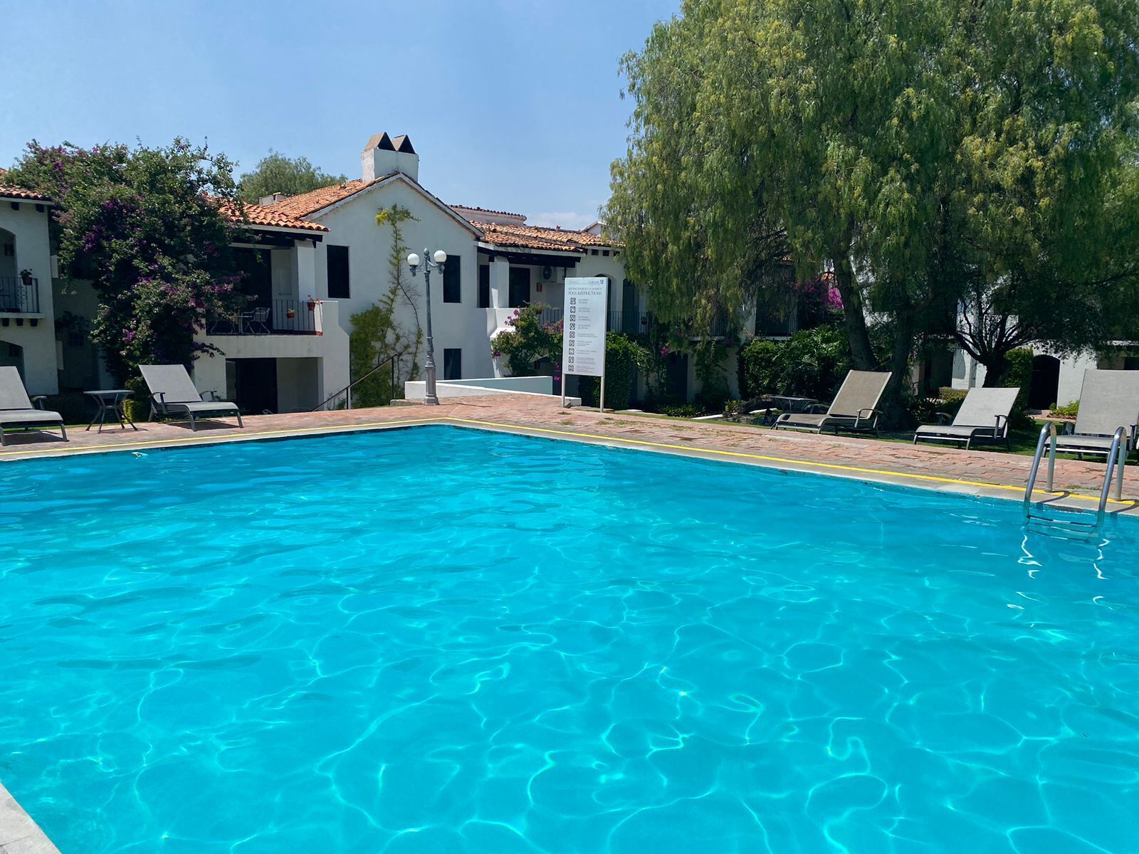 Piscina azul cristalina rodeada de sillones de descanso y un edificio con tejado de azulejos.
