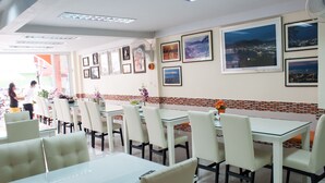 A restaurant with white tables and chairs, framed pictures on the walls, and a tiled backsplash. - At Phuket Inn Patong Beach (Patong)