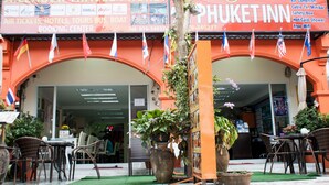 A hotel entrance with a signboard for 'A. Leader Travel Phuket' and 'PHUKET INN'. There are flags hanging above the entrance, and potted plants in front. - At Phuket Inn Patong Beach (Patong)
