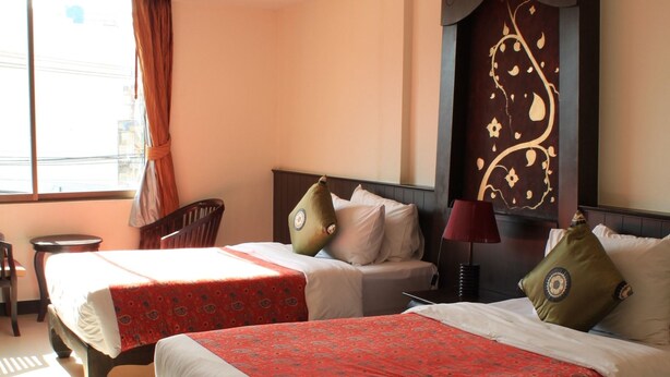 A hotel room with two beds, a sitting area with a chair, a small table, and a decorative wall panel. - At Phuket Inn Patong Beach (Patong)