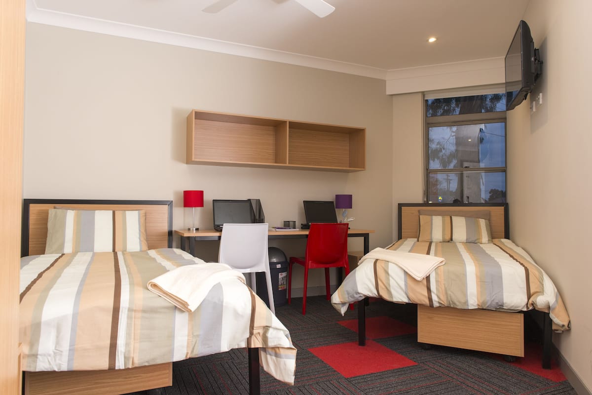 Habitación de hotel con dos camas, un escritorio con computadora, una silla y un televisor montado en la pared.